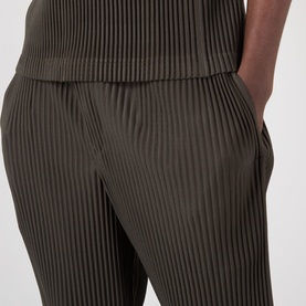 Model wearing Issey Miyake Pleated Wide Leg Trousers in brown, showing elasticated waistband and fine pleated texture detail.