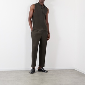 Model wearing Issey Miyake Pleated Wide Leg Trousers in brown with a sleeveless dark top and black loafers.