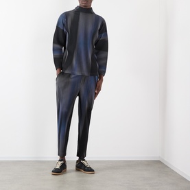 Model wearing Issey Miyake Blend of Lights Pleated Trousers in blue with matching top, styled with black lace-up shoes.