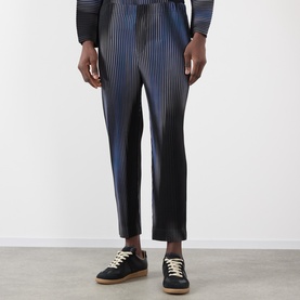 Model wearing Issey Miyake Blend of Lights Pleated Trousers in blue with iridescent pleated detail, styled with black leather trainers.