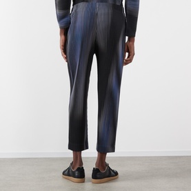 Model wearing Issey Miyake Blend of Lights Pleated Trousers in blue with ombr&eacute; pliss&eacute; texture, styled with a striped top and black loafers.