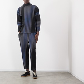 Model wearing Issey Miyake Blend of Lights Pleated Trousers in blue with matching top and black low-top trainers.
