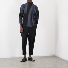 Model wearing Issey Miyake Basic Keshi Pleated Trousers in black, tapered leg, styled with a dark tonal top and black loafers.
