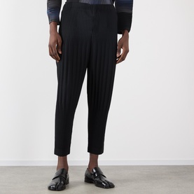 Model wearing Issey Miyake Basic Keshi Pleated Trousers in black, tapered leg with vertical pleats, styled with patent loafers.