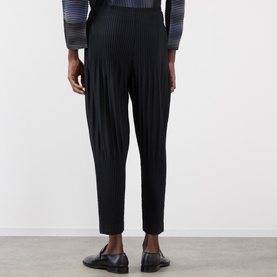 Model wearing Issey Miyake Basic Keshi Pleated Trousers in black, tapered leg with elasticated waist, styled with black loafers.