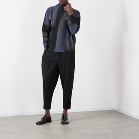 Model wearing Issey Miyake Basic Keshi Pleated Trousers in black, tapered leg with keshi pleats, styled with a dark knit sweater and loafers.