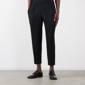Model wearing Issey Miyake Pleated Wide Leg Trousers in black, with elasticated waist and pleated legs, styled with black patent loafers.