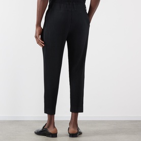 Model wearing Issey Miyake Pleated Wide Leg Trousers in black, elasticated waist, cropped length, styled with black loafers.