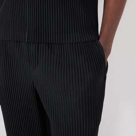 Model wearing Issey Miyake Pleated Wide Leg Trousers in black, showing elasticated waist and textured pleated leg detail.