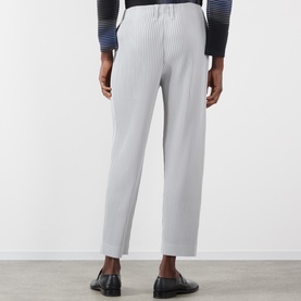 Model wearing Issey Miyake Pleated Wide Leg Trousers in grey, shown from behind, styled with a striped top and black loafers.