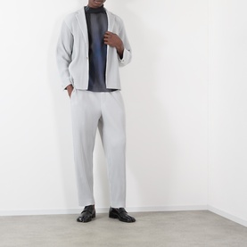 Model wearing Issey Miyake Pleated Wide Leg Trousers in grey, styled with matching grey jacket and dark rollneck top.