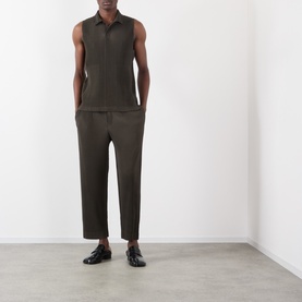 Model wearing Issey Miyake Pleated Polo Shirt in brown, sleeveless with polo collar, styled with matching brown pleated trousers and black loafers.