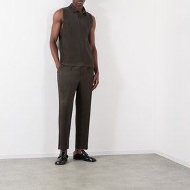 Model wearing Issey Miyake Pleated Polo Shirt in brown, sleeveless with polo collar, styled with dark trousers and black leather shoes.