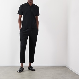 Model wearing Issey Miyake Open Collar Pleated Polo Shirt in black with matching black trousers and patent loafers.