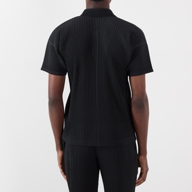 Model wearing Issey Miyake Open Collar Pleated Polo Shirt in black, shown from behind, with matching black pleated trousers.