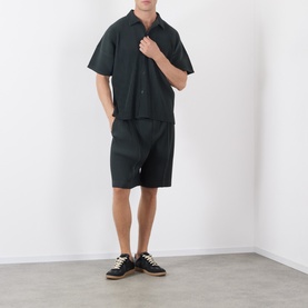 Model wearing Issey Miyake Special Black polyester shorts with matching short-sleeve shirt and black canvas trainers.