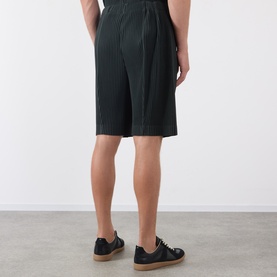 Model wearing Issey Miyake shorts in Special Black, pleated textured fabric, shown from behind, styled with beige canvas trainers.