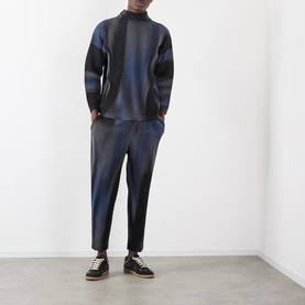 Model wearing Issey Miyake Gradient Pleated T-Shirt in blue with abstract stripe gradation, styled with matching pleated trousers and black trainers.