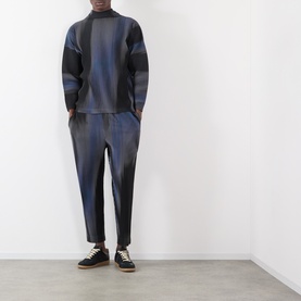 Model wearing Issey Miyake Gradient Pleated T-Shirt in blue with abstract stripe gradation and high neck, styled with matching pleated trousers and
