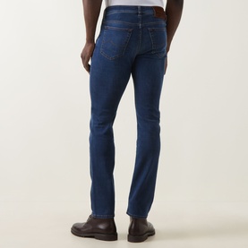 Model wearing Jacob Cohen Bard Slim Leg Jeans in medium blue with tobacco stitching and leather logo patch, rear view, styled with brown leather