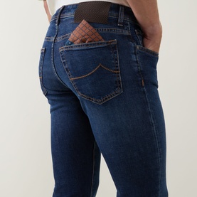 Model wearing Jacob Cohen 3049 slim jeans in dark blue denim, rear view showing branded back pockets with brown leather patch detail.