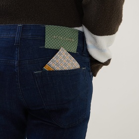 Model wearing dark blue slim-fit jeans with a patterned pocket square in back pocket, styled with a dark knit top