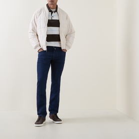 Model wearing white quilted puffer jacket styled with brown striped polo, dark navy jeans, and brown leather trainers