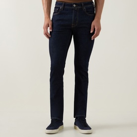 Model wearing Jacob Cohen 3049 slim jeans in dark blue denim, styled with white trainers. Five-pocket design with contrast stitching.
