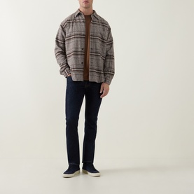 Model wearing Jacob Cohen 3049 slim jeans in dark blue, styled with a brown plaid overshirt and navy canvas shoes