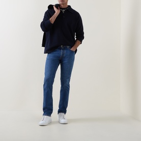 Model wearing Jacob Cohen 3049 slim jeans in medium blue, styled with a navy knit and white trainers.
