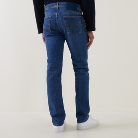 Model wearing Jacob Cohen 3049 slim jeans in medium blue denim, rear view, styled with white trainers and navy top.