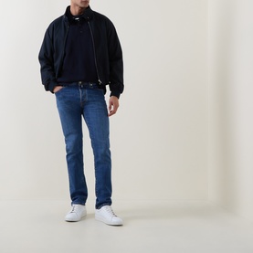 Model wearing Jacob Cohen 3049 slim jeans in medium blue, styled with a navy bomber jacket and white trainers.