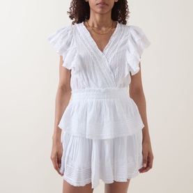 Model wearing LOVESHACKFANCY Gwen Heritage Mini Dress in white with flutter sleeves, wrap V-neckline, tiered skirt and embroidered detailing