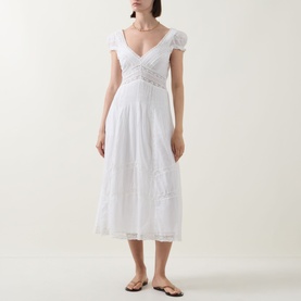 Model wearing LOVESHACKFANCY Suvi Lace Trim Flared Dress in white, midi length with V-neckline, cap sleeves and lace trim detail. Styled with tan