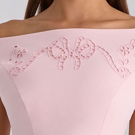 Model wearing House of CB pink top with laser-cut bow and floral embroidery detail at neckline, off-shoulder style