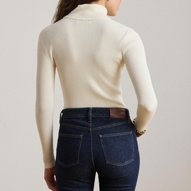 Model wearing Lauren mascarpone cream ribbed turtleneck jumper, back view, styled with dark blue jeans and gold bracelet.