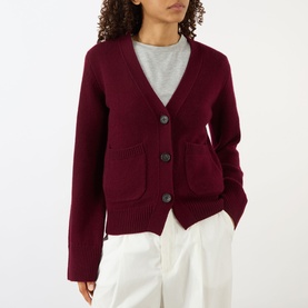 Model wearing Lisa Yang Deep Plum cashmere cardigan with V-neck, button front and patch pockets, styled with grey top and white trousers.