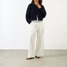 Model wearing Lisa Yang navy cashmere cardigan with cable-knit texture, styled with white wide-leg trousers and brown flat sandals.