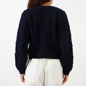 Model wearing Lisa Yang navy cashmere cable-knit cardigan, back view, styled with white wide-leg trousers