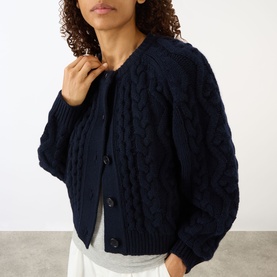 Model wearing Lisa Yang navy cashmere cable-knit cardigan with button fastening, styled with white trousers