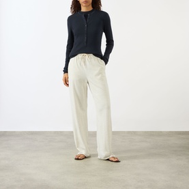 Model wearing Lisa Yang Airi Navy Cashmere Polo Shirt with long sleeves and half-button placket, styled with cream wide-leg trousers and tan sandals.