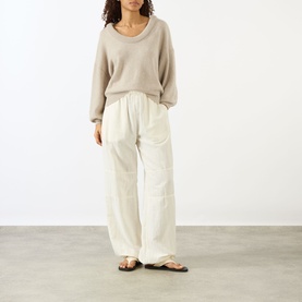 Model wearing Lisa Yang The Doria Cashmere Sweater in Sand, scoop neck, long sleeves, styled with wide-leg cream trousers and flat sandals.