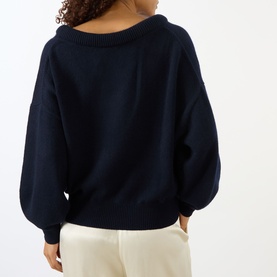 Model wearing Lisa Yang The Doria Cashmere Sweater in navy, back view showing scoop neck, balloon sleeves and ribbed trims, styled with cream trousers