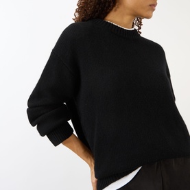 Model wearing Lisa Yang black cashmere knit sweater with crew neck, styled over white layered top