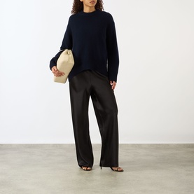 Model wearing Lisa Yang Noor Cashmere Sweater in navy with black wide-leg trousers and heeled sandals, carrying a cream clutch bag.