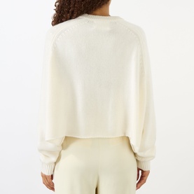 Model wearing Lisa Yang The Karine Sweater in cream, showing rear view with dropped shoulders, ribbed trims, and long sleeves. Styled with cream