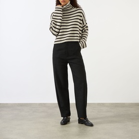 Model wearing Lisa Yang Zerlina Striped Turtleneck Sweater in Oyster/Dark Oak Stripes, styled with black wide-leg trousers and loafers.