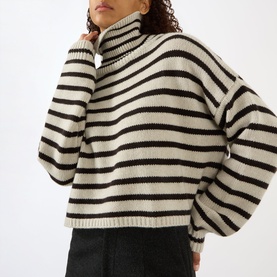 Model wearing Lisa Yang Zerlina Striped Turtleneck Sweater in Oyster and Dark Oak stripes, with ribbed trims and relaxed fit, styled with black
