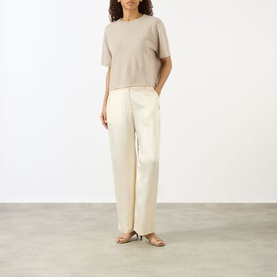 Model wearing Lisa Yang sand cashmere T-shirt with cream wide-leg trousers and tan strappy flat sandals.