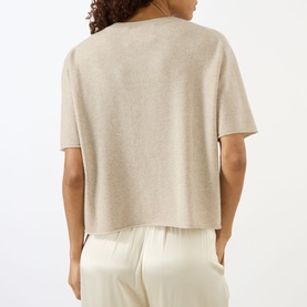 Model wearing Lisa Yang sand cashmere T-shirt, rear view, relaxed boxy fit with short sleeves, styled with cream wide-leg trousers.
